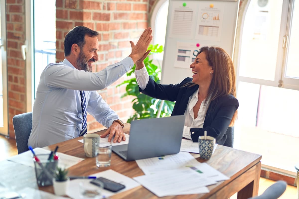 Two business professionals high-fiving over a laptop and paperwork
