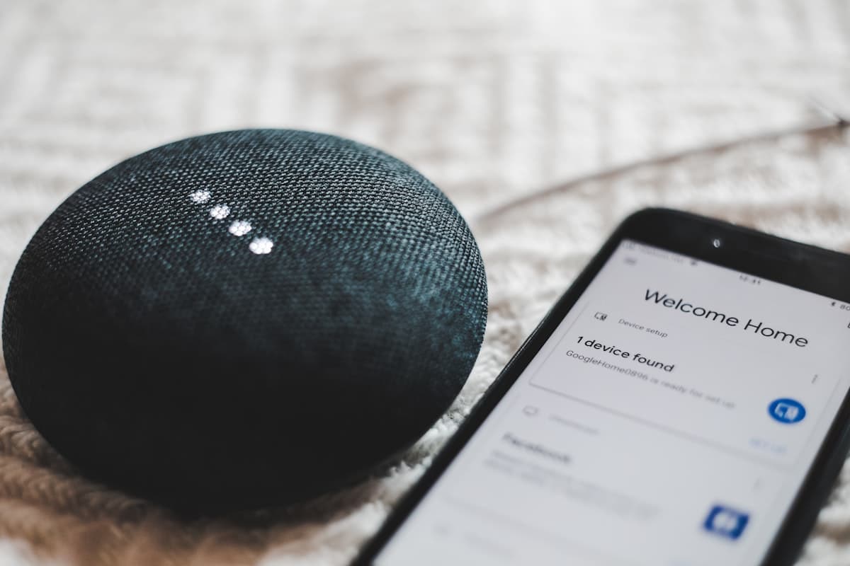 A smart speaker beside a smartphone showing a device setup screen