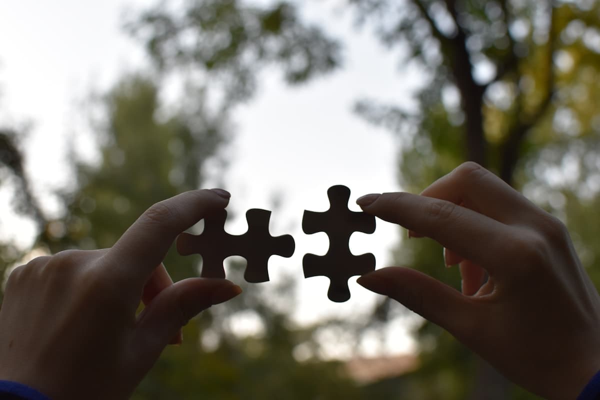 Two hands connecting two puzzle pieces against a sky backdrop