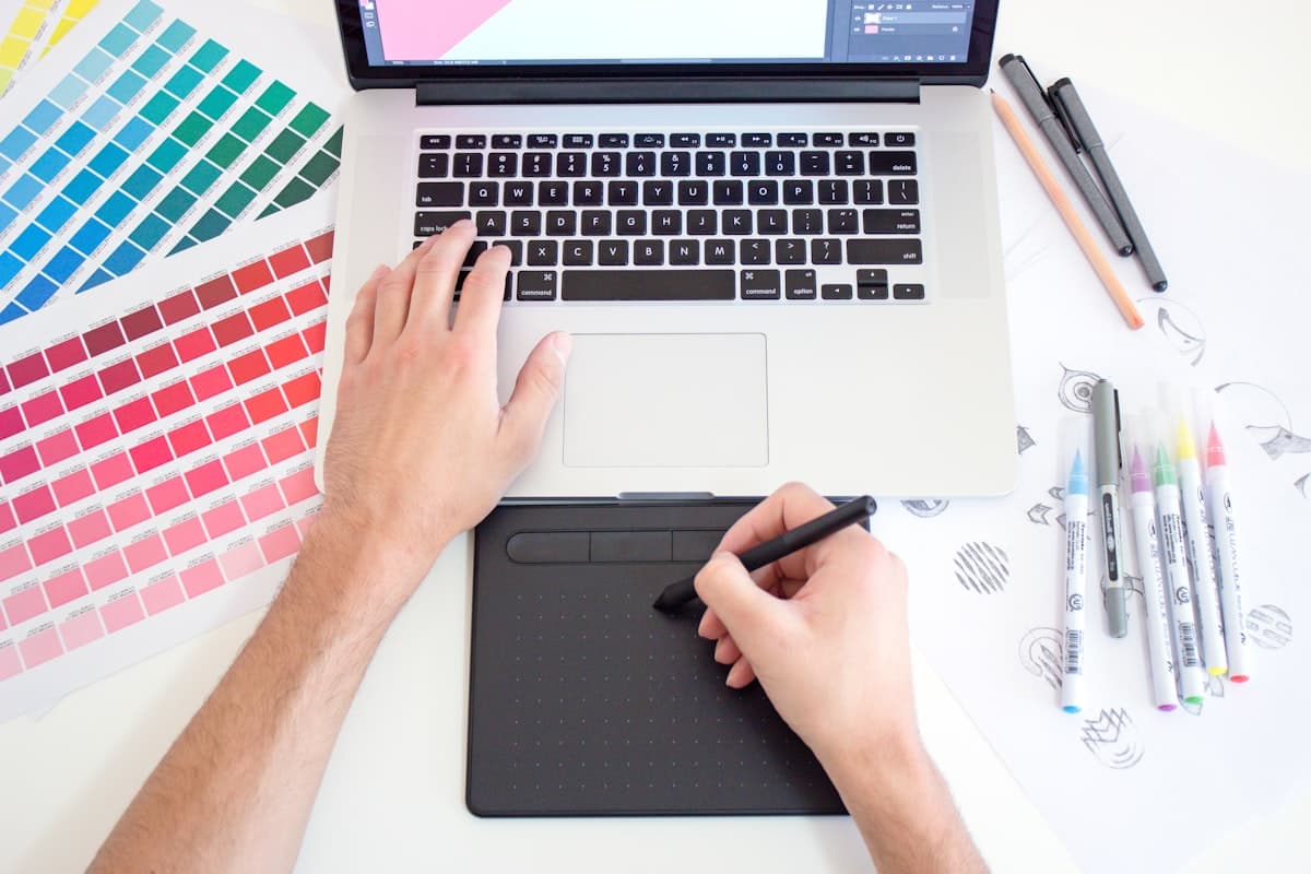 A designer's workspace with color swatches, sketches, a drawing tablet, and a laptop