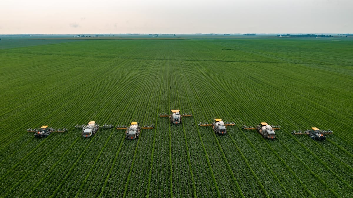 Aerial view of agricultural sprayers moving through a green field