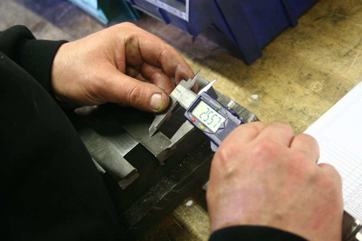 Hands using a digital caliper to precisely measure a metal component