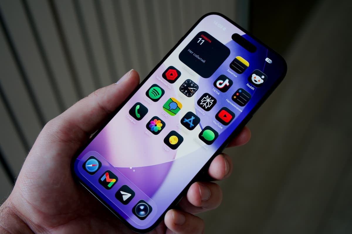 A hand holding a smartphone displaying app icons