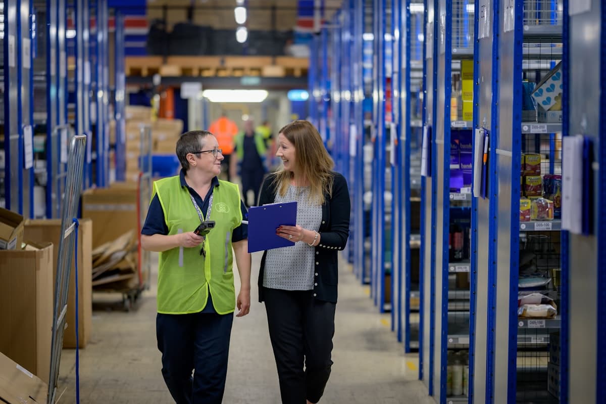 Two logistics workers walking through a warehouse aisle
